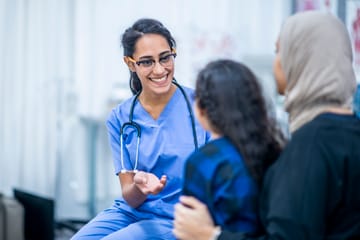 Female health care worker wearing a stethoscope and talking with a woman and her daugher
