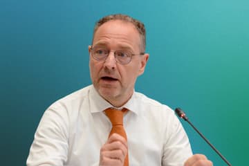 Portrait of Paolo Bernasconi Man speaking at microphone with blue-green background.