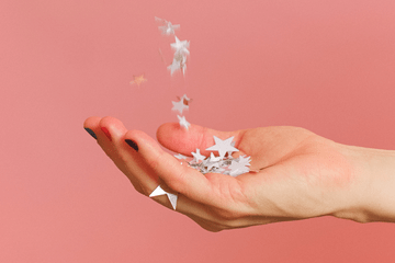 Hand holding falling stars on pink background.