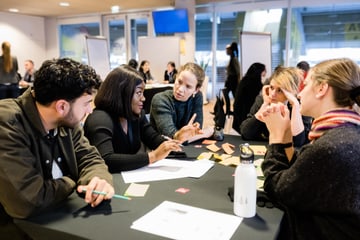 Five people having a discussion around a table with papers and sticky notes.