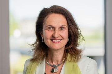 Smiling woman in white jacket and green scarf indoors.