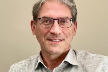 Man with glasses smiling, wearing gray shirt.