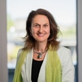 Smiling woman in white jacket and green scarf indoors.